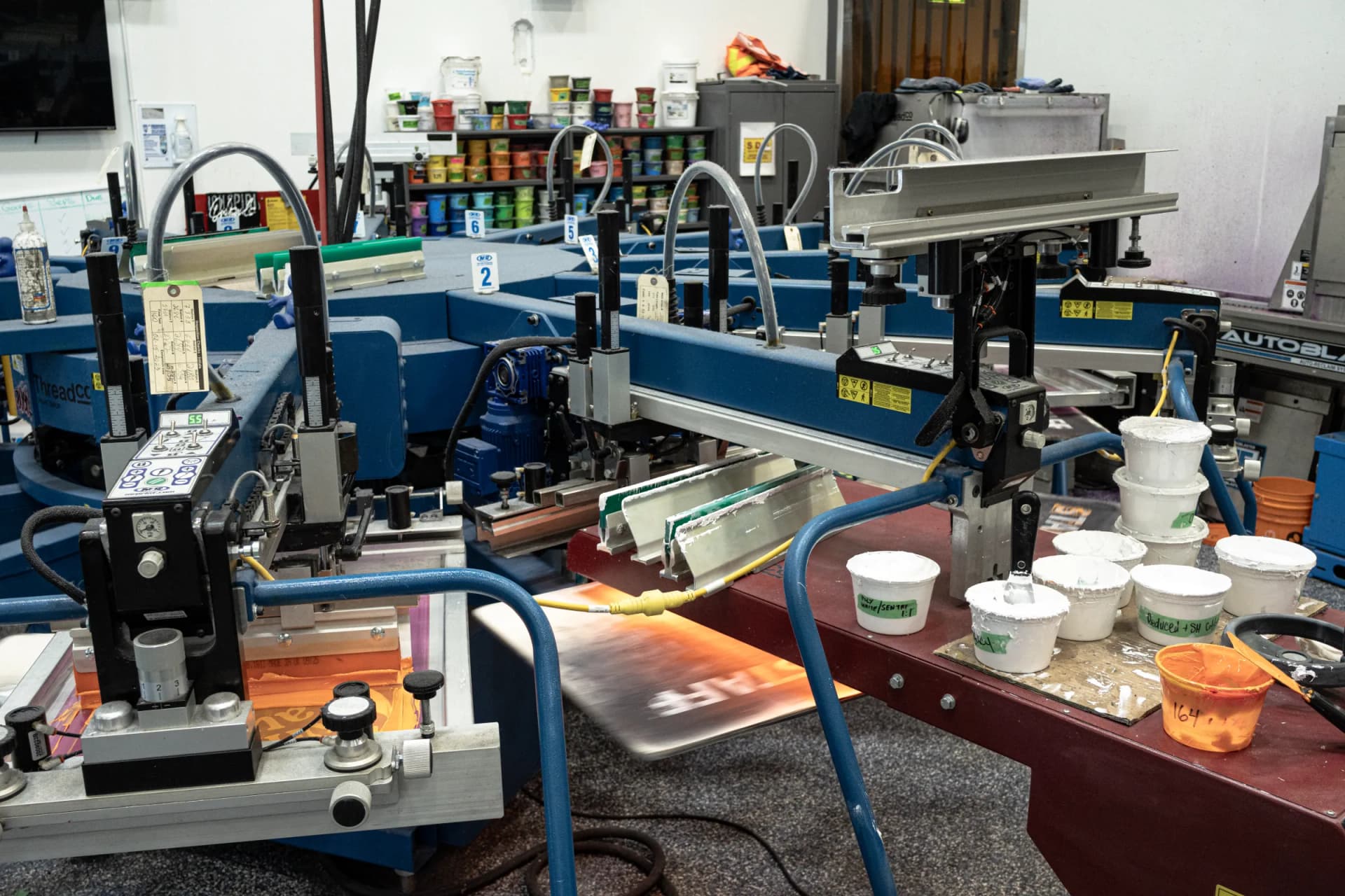 Squeegees and tubs of white ink on the automatic screen-printing press at ThreadCo Print Shop in Vancouver
