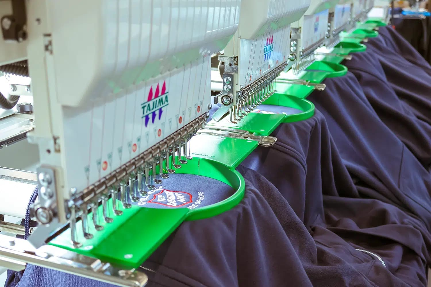 Multi-head embroidery machine stitching a crest on a row of navy jackets at ThreadCo Print Shop, Vancouver